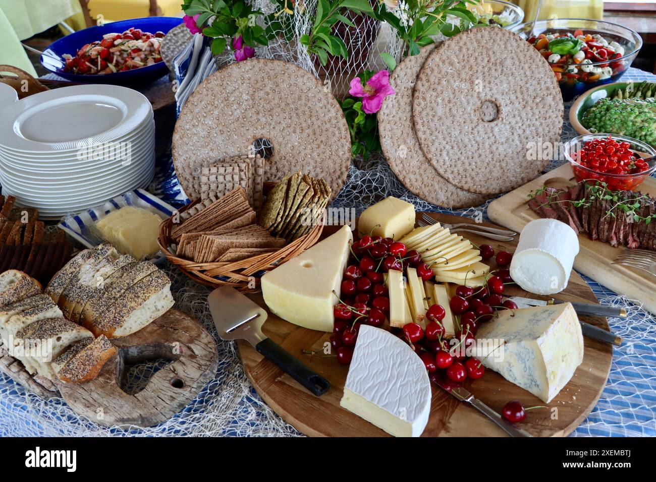 Tagliere di formaggi con selezione di formaggi e pane croccante, decorato con ciliegie su buffet di mezza estate, giugno 2024 Foto Stock