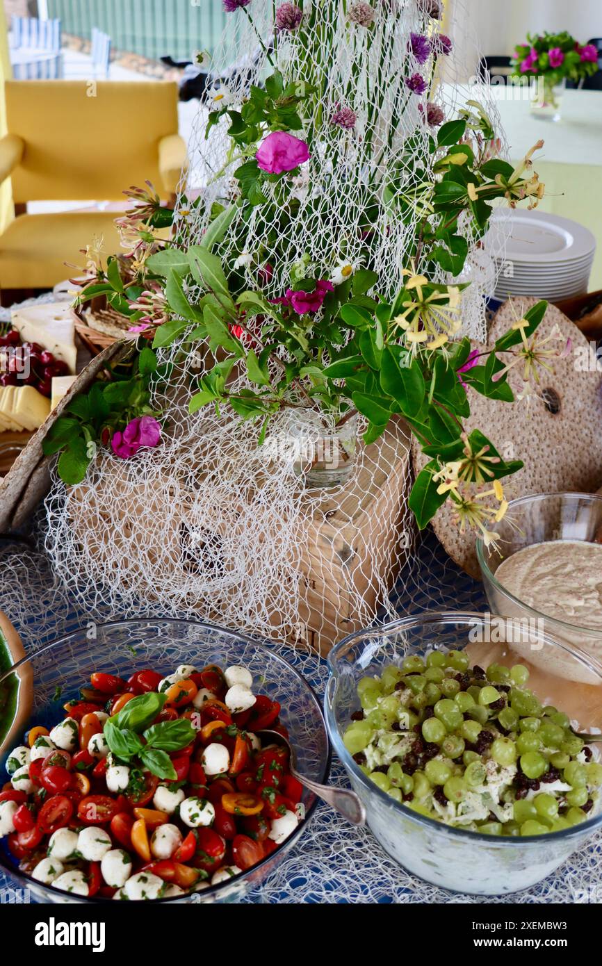 Insalata di mozzarella e insalata Waldorf a cena a buffet decorata con vecchia rete da pesca, rose selvatiche e fiori di cipolla selvatica. Midsummer in Svezia, giugno 2024 Foto Stock