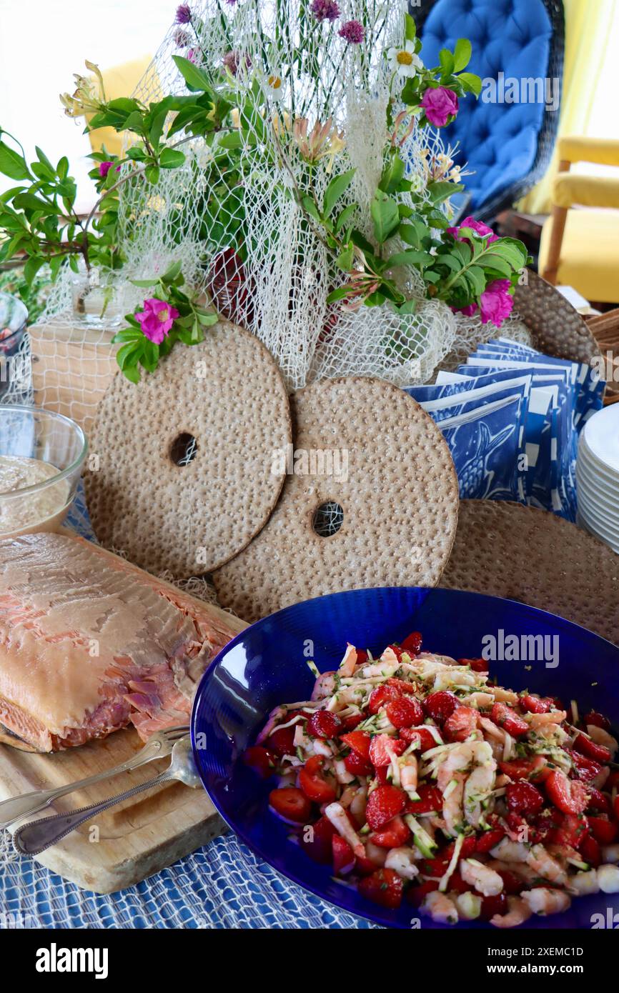 Insalata di salmone e gamberi affumicati a caldo per cena a buffet decorata con vecchia rete da pesca, rose selvatiche e fiori di cipolla selvatica. Midsummer in Svezia, giugno 2024 Foto Stock