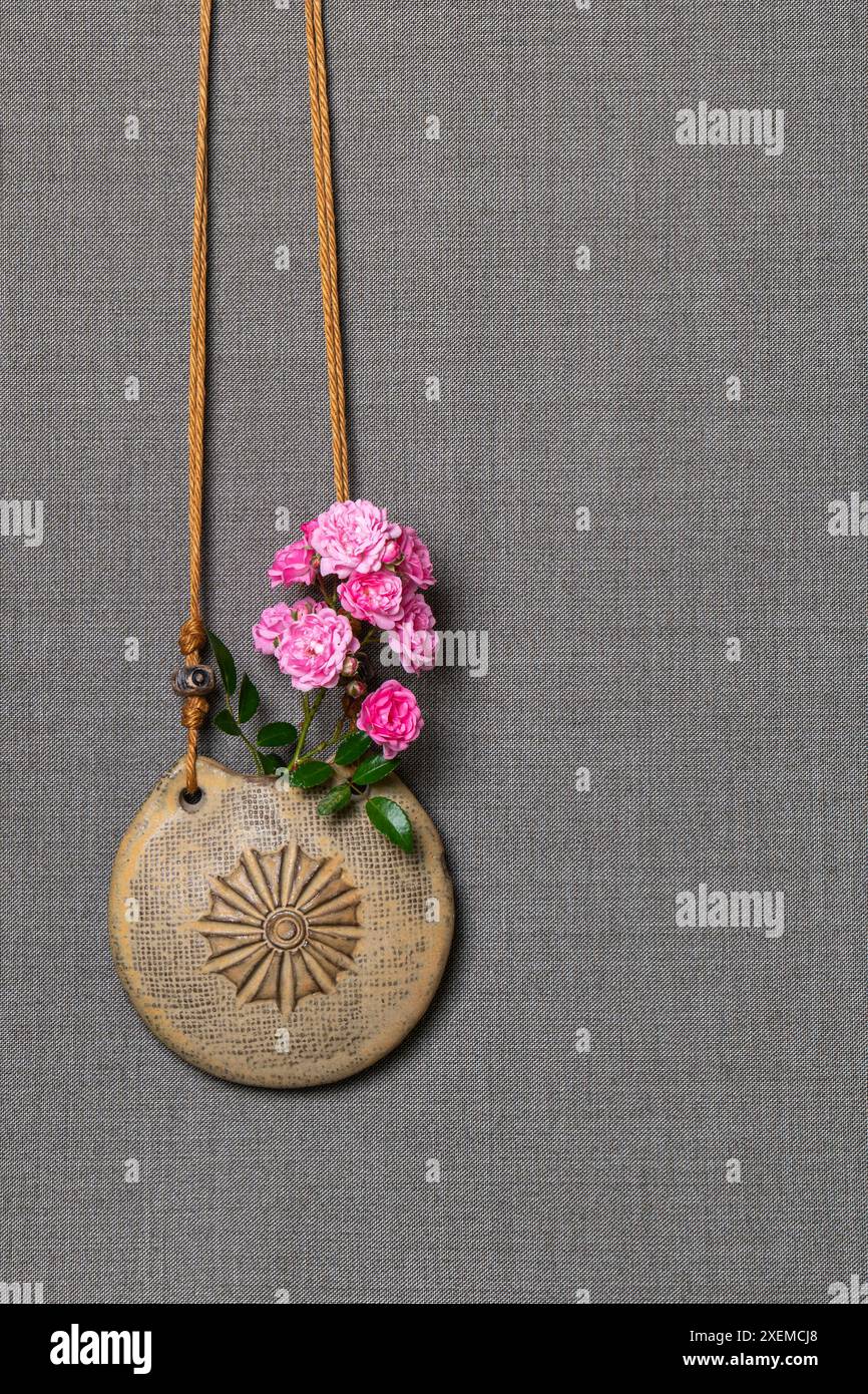 Vaso rotondo appeso con un ornamento. Contiene un piccolo bouquet di rose rosa. Corda. Sfondo grigio. Cartolina. Posiziona per testo. Auguri per le vacanze. Foto Stock