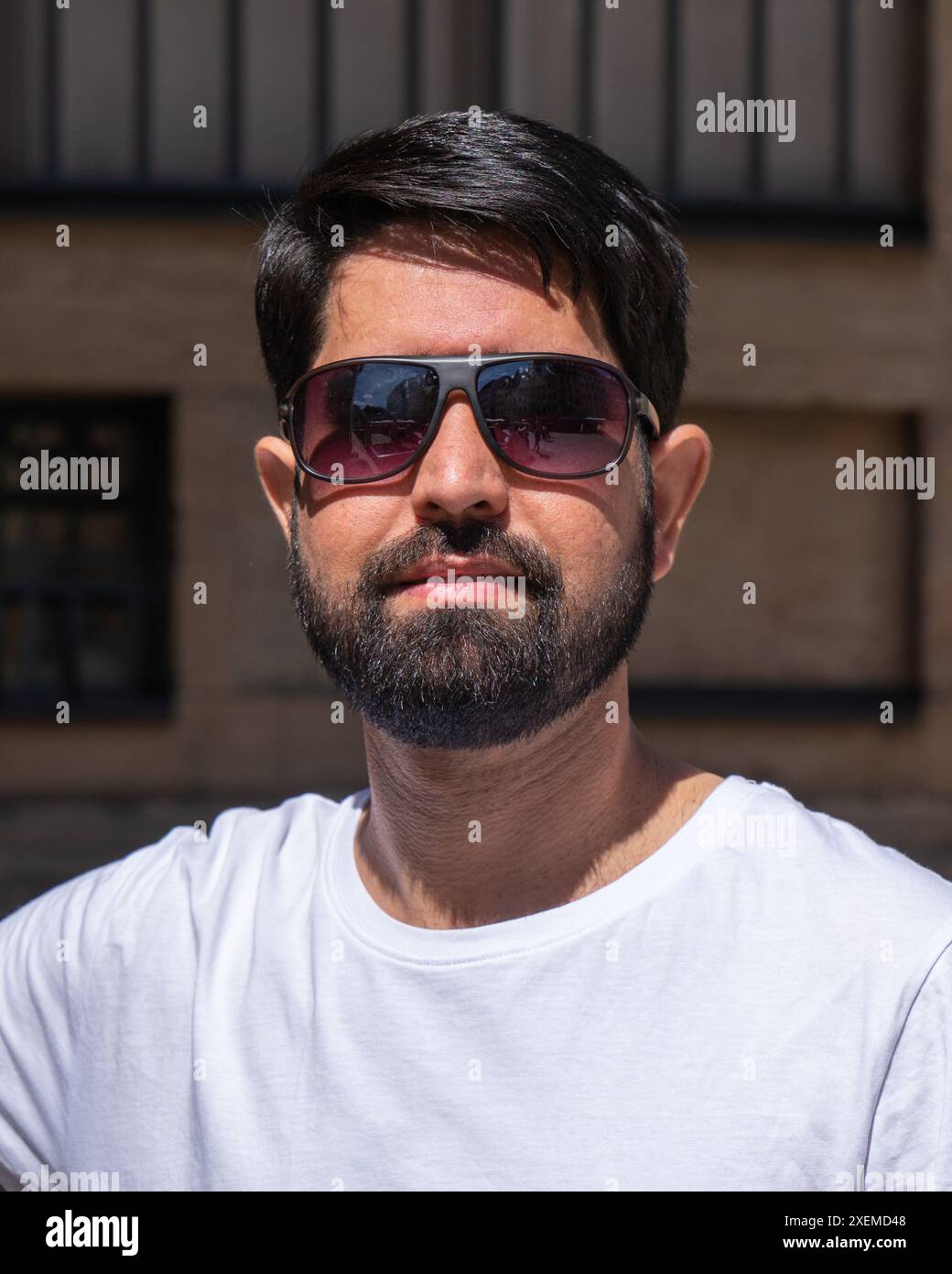 Ritratto ravvicinato di un moderno pakistano con barba scura, vestiti chiari e occhiali da sole Foto Stock