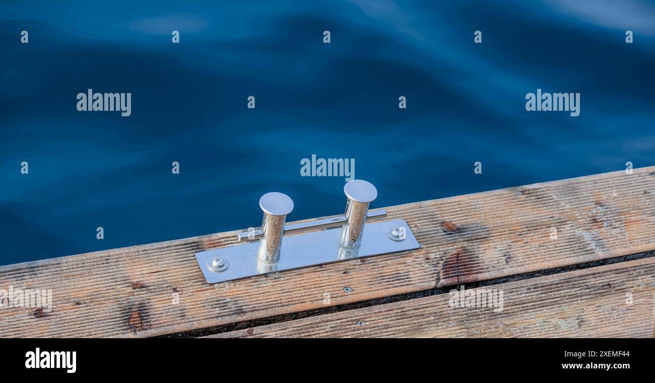 Supporto in metallo per ormeggio barche (dissuasore in acciaio inox) su una piattaforma in legno vicino a un corpo d'acqua. Foto Stock