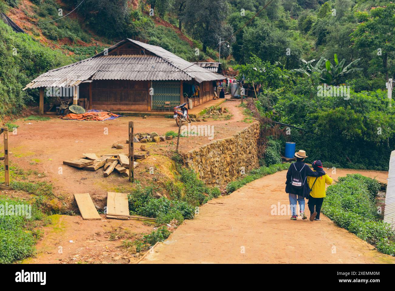 Due donne camminano lungo una strada sterrata in Vietnam, una con il braccio intorno all'altra; Ban Nam Nghiep, Muong la, Son la, Vietnam Foto Stock