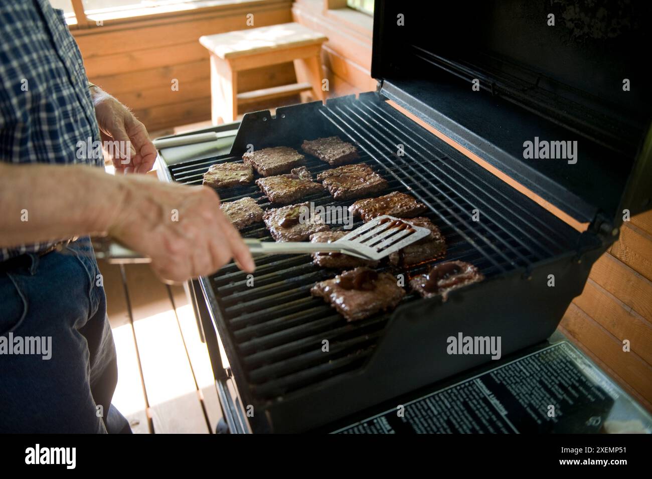 L'uomo anziano cucina hamburger su una griglia.; Elkhorn, Nebraska, Stati Uniti d'America Foto Stock