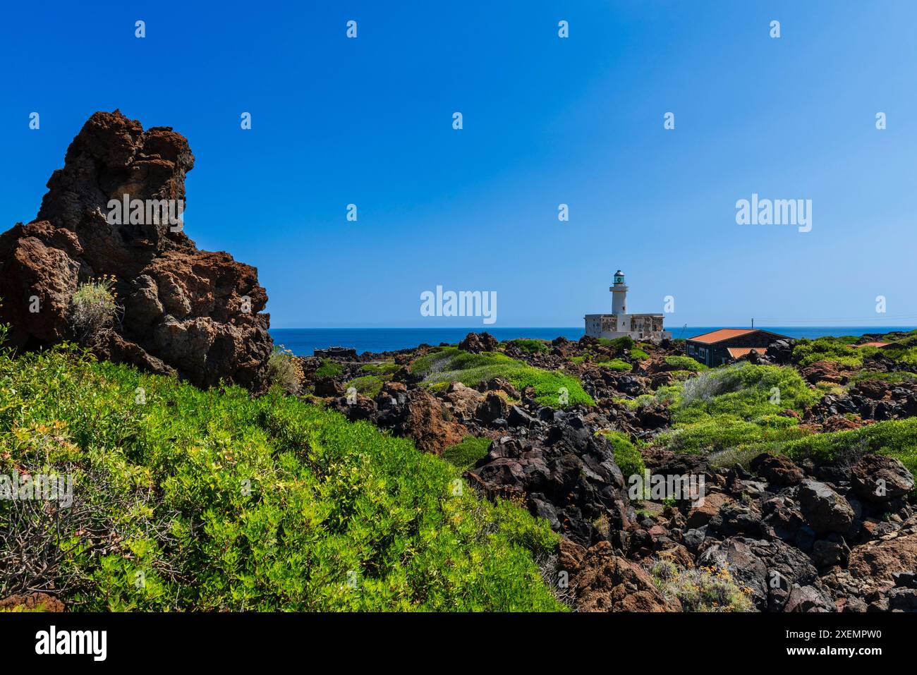 Vista panoramica del paesaggio costiero con formazioni rocciose vulcaniche e il Faro di Faro di Punta Spadillo nel Parco Nazionale di Pantelleria... Foto Stock