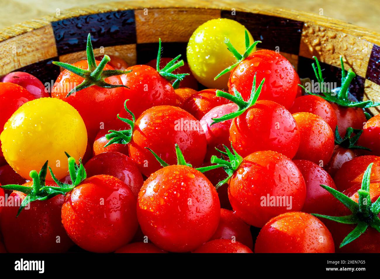 Primo piano di pomodori ciliegini multicolori (Solanum lycopersicum var. cerasiforme) con goccioline d'acqua in una ciotola di legno Foto Stock