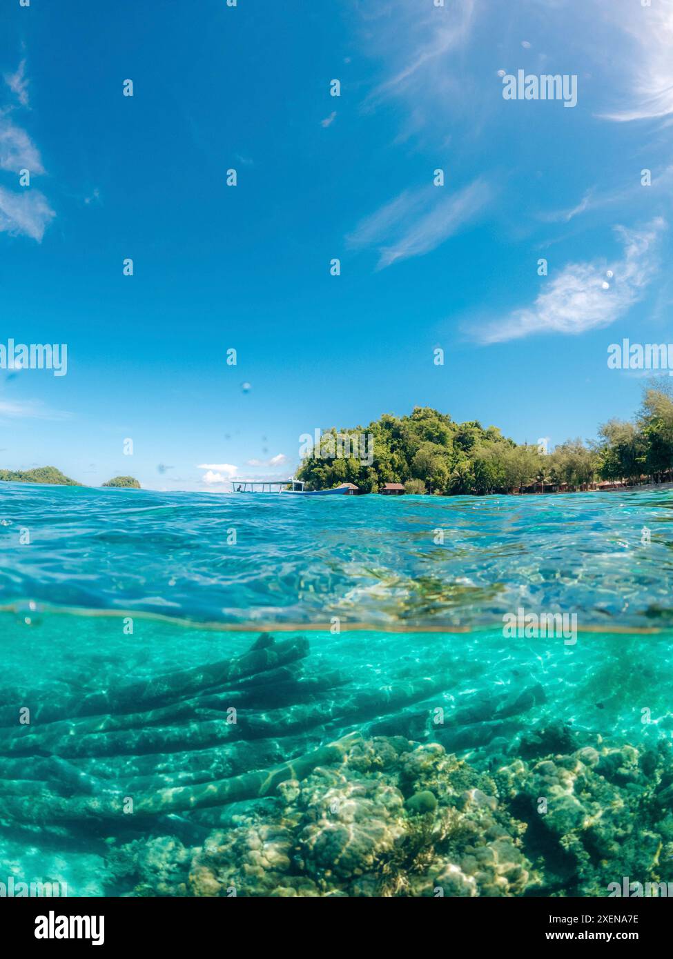 Vista divisa di una barriera corallina nelle acque cristalline dell'oceano turchese e sulla costa con barca nel Parco Nazionale Kepulauan Togean; Wakai, Sulawesi centrale, Indonesia Foto Stock