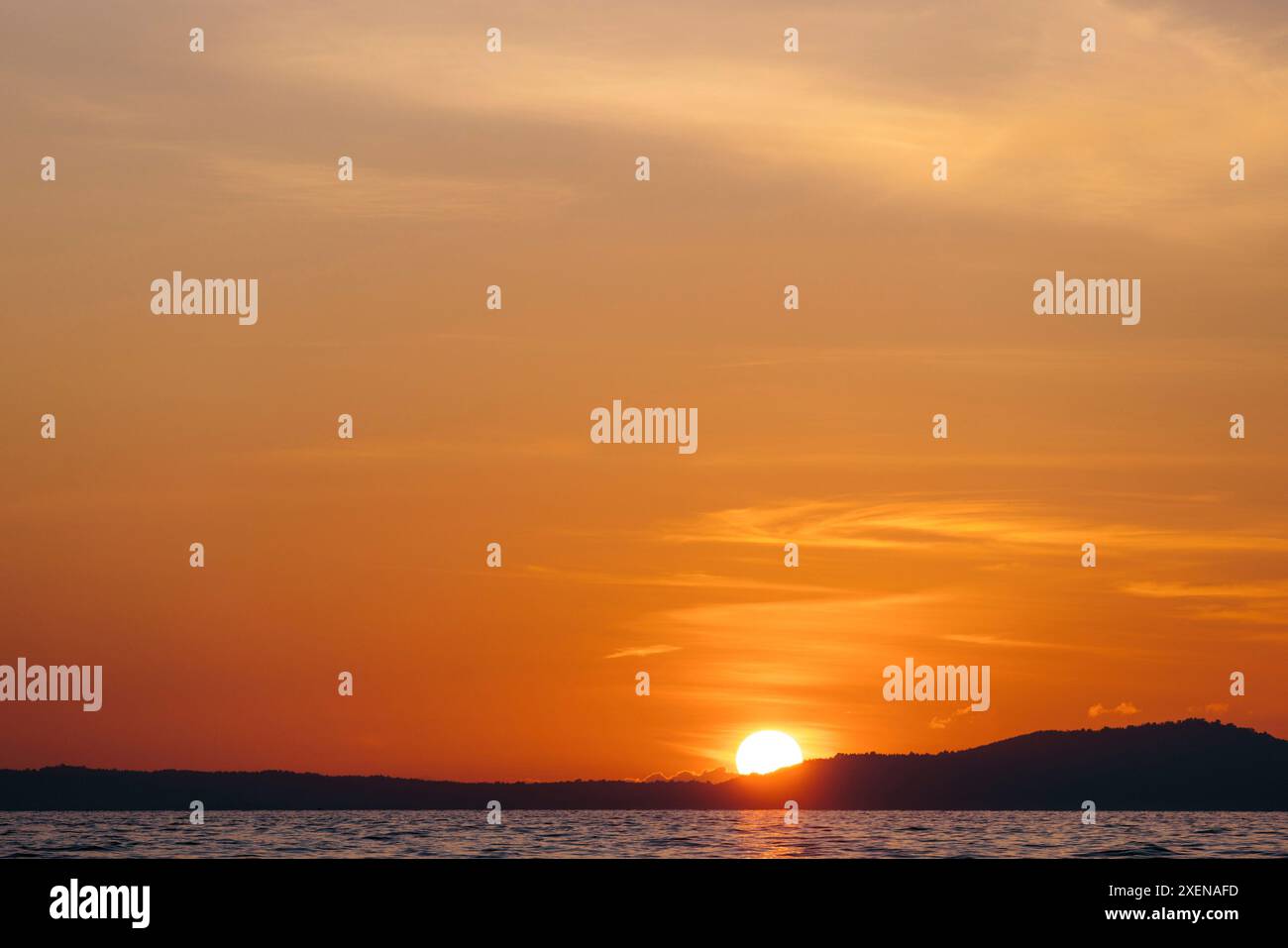 Sole incandescente che affonda dietro l'orizzonte sull'isola sagomata di Bunaken nel Mare di Celebes, Indonesia; Bunaken, Sulawesi settentrionale, Indonesia Foto Stock