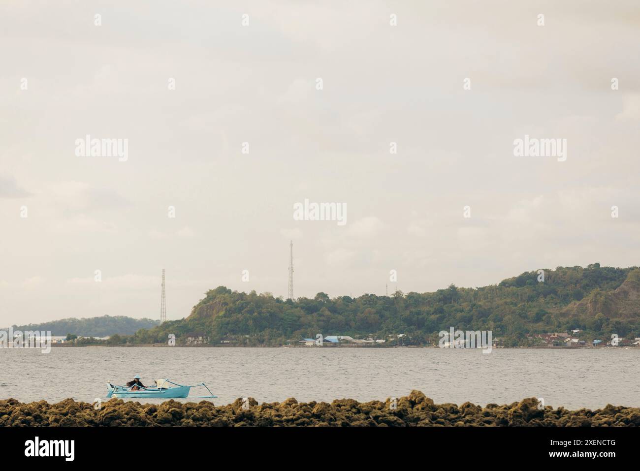 Pescatore che pesca dal suo piccolo gonfiore lungo il litorale vicino all'isola di Dutungan sullo stretto di Makassar in Indonesia Foto Stock