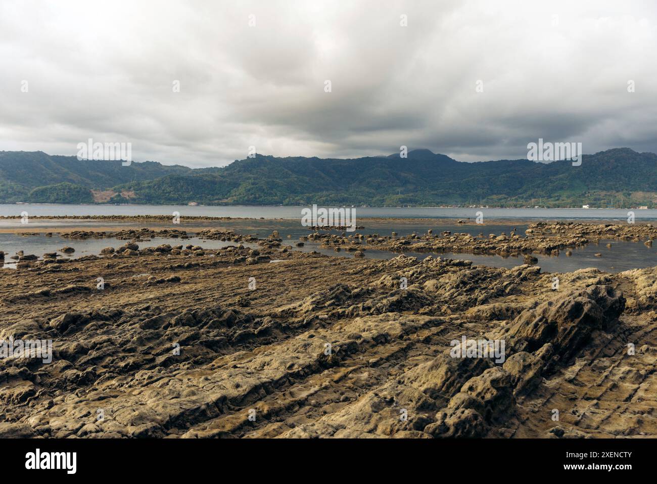 Vista dell'isola di Dutungan e della lussureggiante vegetazione lungo la costa sotto un cielo coperto Foto Stock