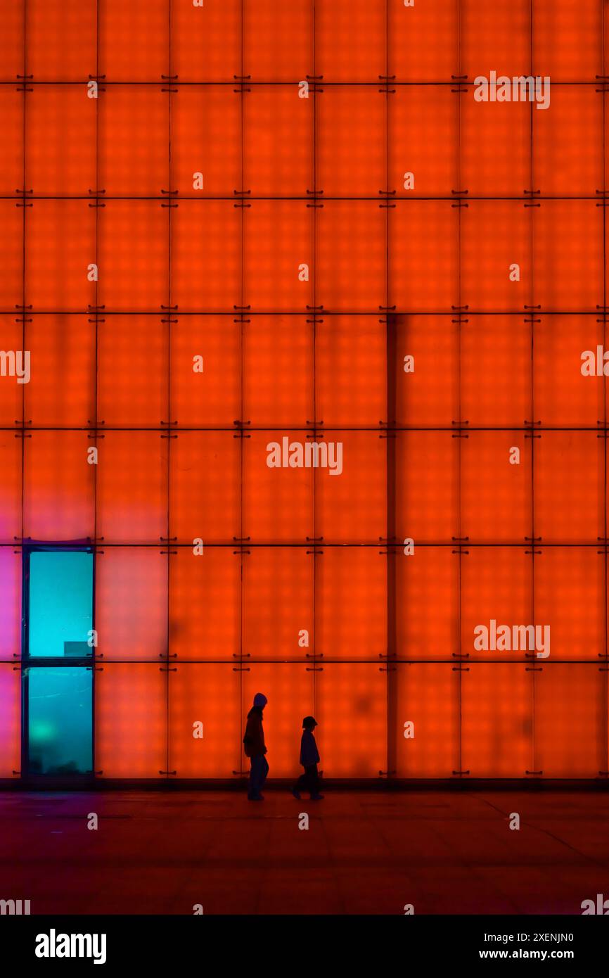 Una famiglia che cammina attraverso le pareti illuminate del grande teatro di Chongqing di notte, una scena astratta ma cyberpunk. Foto Stock