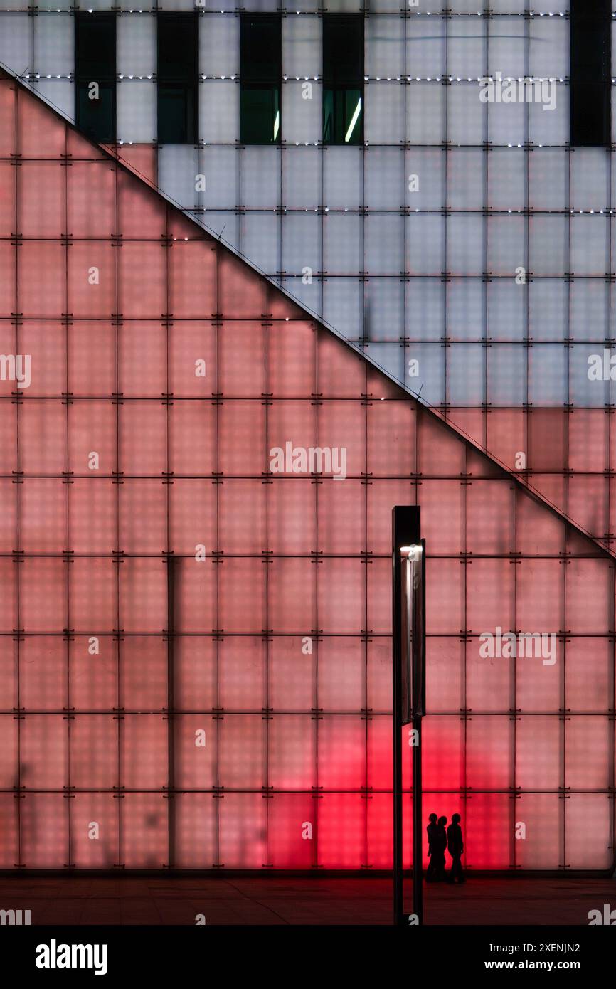 Una famiglia che cammina attraverso le pareti illuminate del grande teatro di Chongqing di notte, una scena astratta ma cyberpunk. Foto Stock