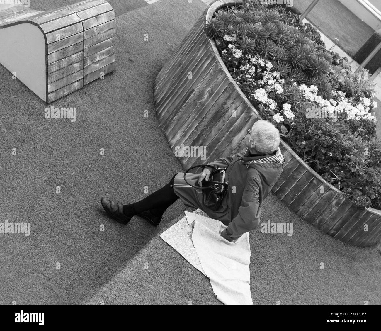 Una donna anziana siede da sola in uno spazio pubblico Foto Stock