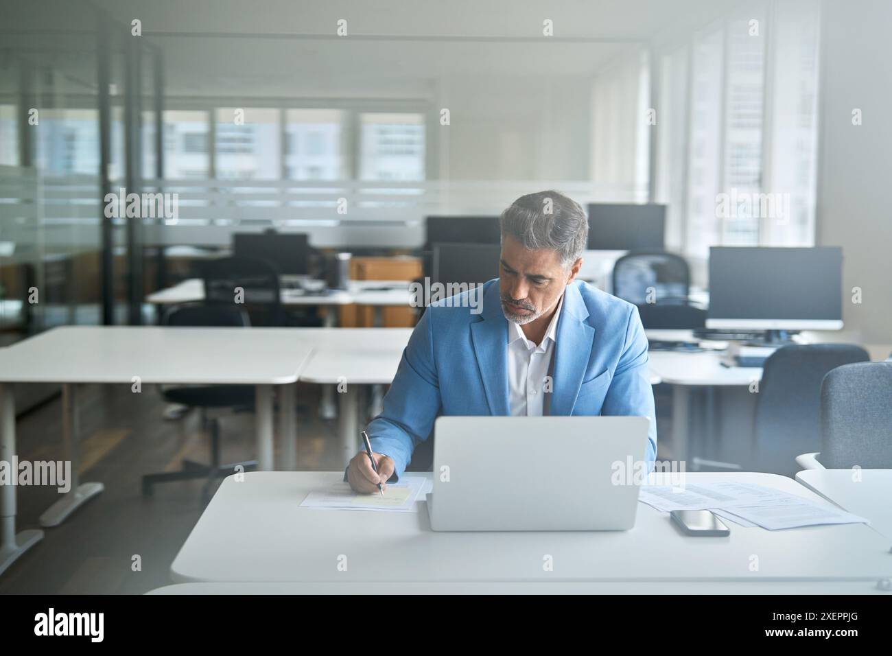 Uomo d'affari di mezza età impegnato che lavora su un notebook in ufficio per scrivere appunti. Foto Stock