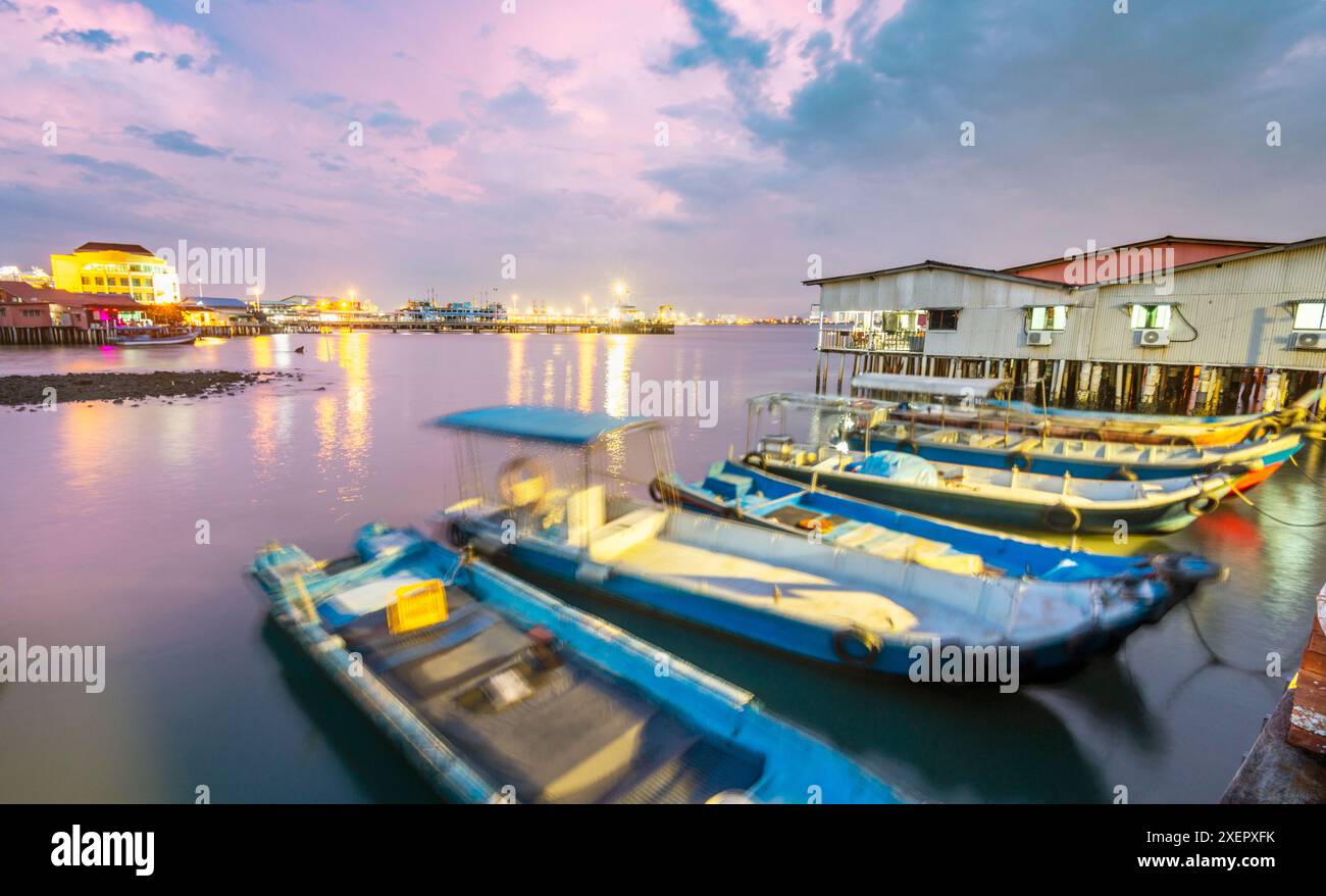 Bellissimi cieli rosa, piccole barche che ormeggiano nelle calme acque del mare dello stretto di Malacca e vecchi edifici in legno, illuminati lungo la passerella di DUS Foto Stock