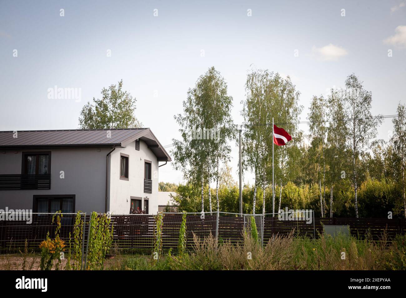 Questa immagine mostra una moderna casa unifamiliare situata in un tranquillo quartiere residenziale di una città lettone. La casa è circondata dalla natura, wi Foto Stock