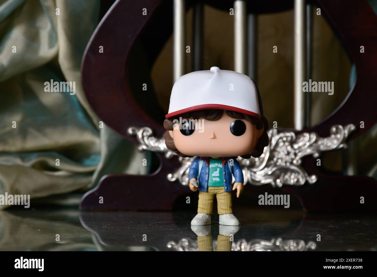 Funko Pop action figure di Dustin Henderson della popolare serie TV di Netflix Stranger Things. Pavimento riflettente, tenda verde, gabbia vintage, colonne. Foto Stock