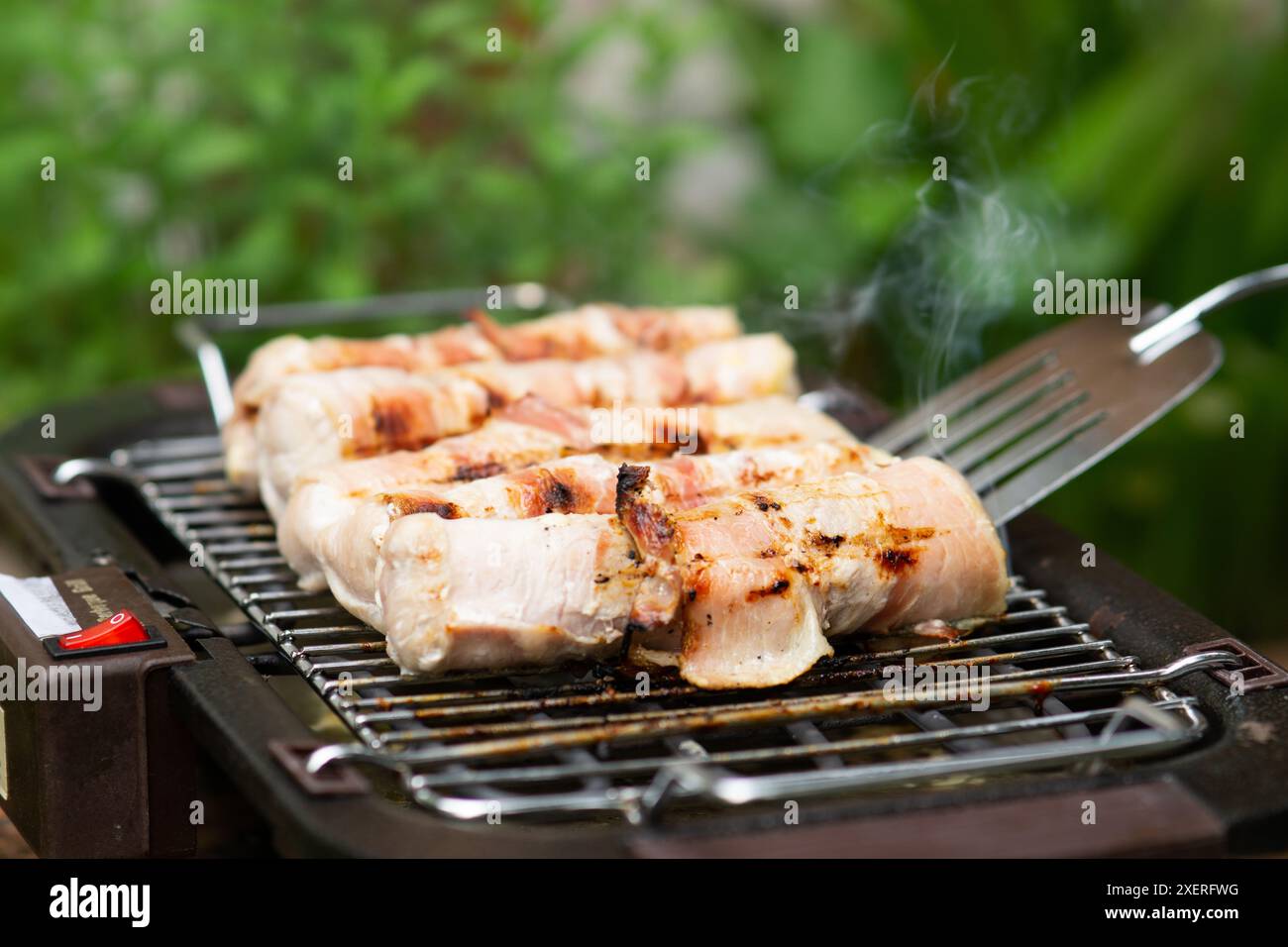 Uomo che grigia capovolgendo la carne sulla griglia del barbecue nel suo cortile. primo piano di un uomo che prepara barbecue nel suo cortile, un uomo usa le pinze per capovolgere un grigliato Foto Stock