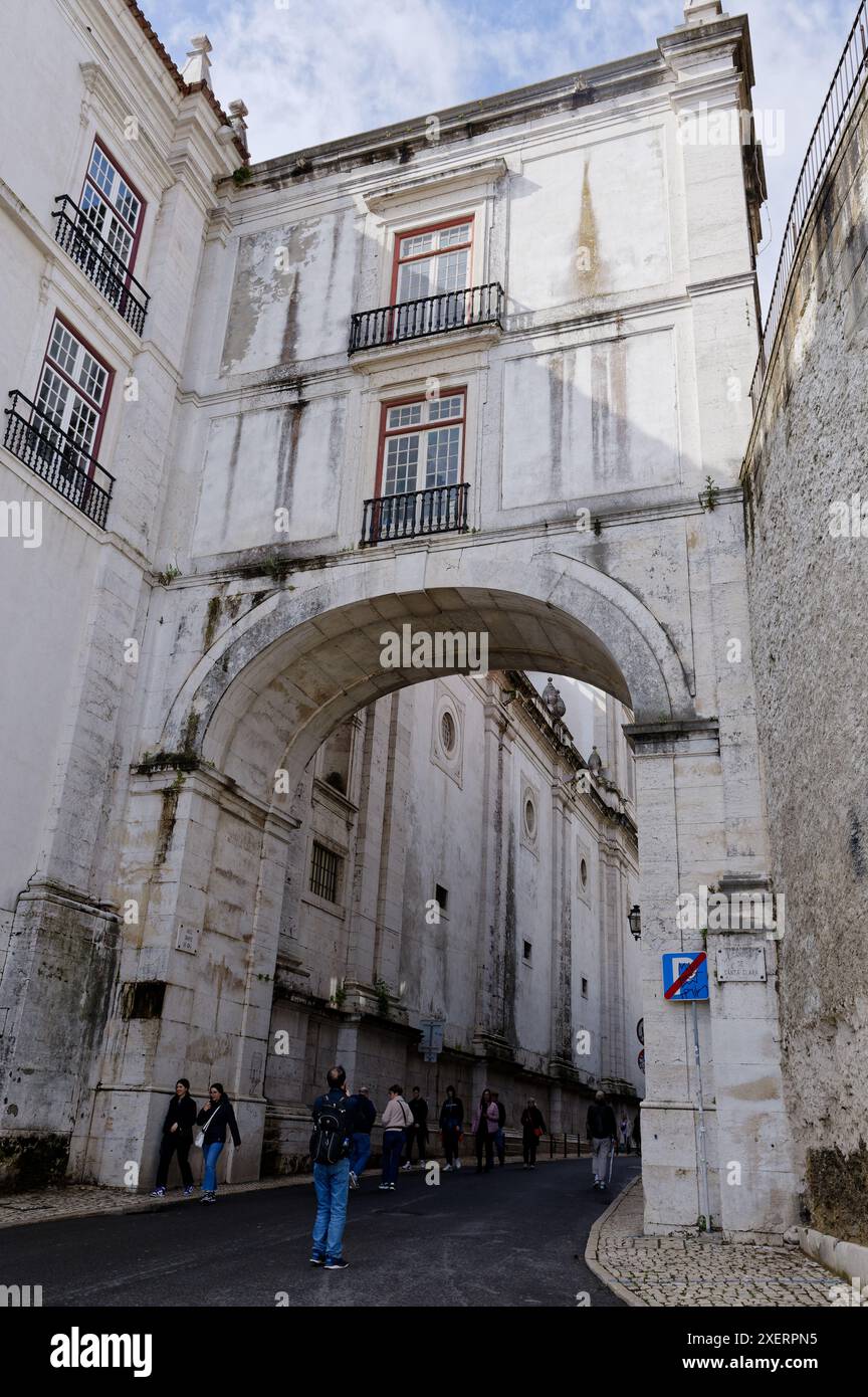 I turisti camminano sotto l'arco grande de cima del monastero di São vicente de fora, circondato dalle mura di pietra della città vecchia Foto Stock