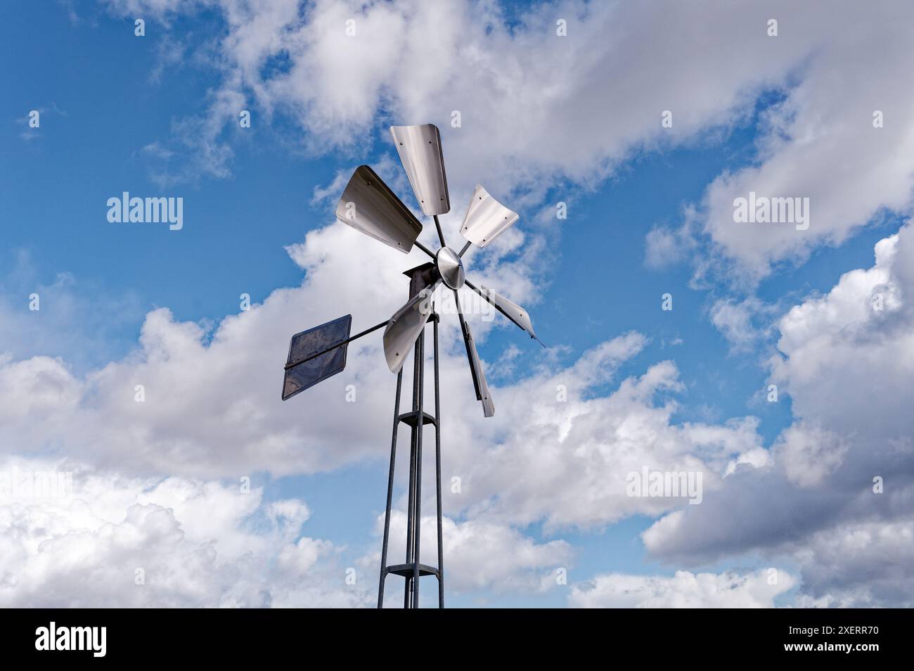 Il mulino a vento in metallo si erge alto su uno sfondo di soffici nuvole e le sue lame catturano la luce a Lisbona Foto Stock