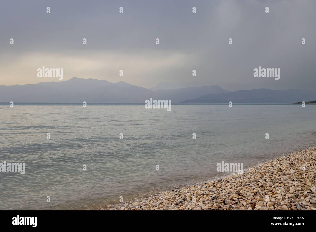 Mare calmo durante un tramonto a tarda primavera. Cielo nuvoloso. Costa dell'Albania con alte montagne all'orizzonte. Acharavi, Korfu, Grecia. Foto Stock