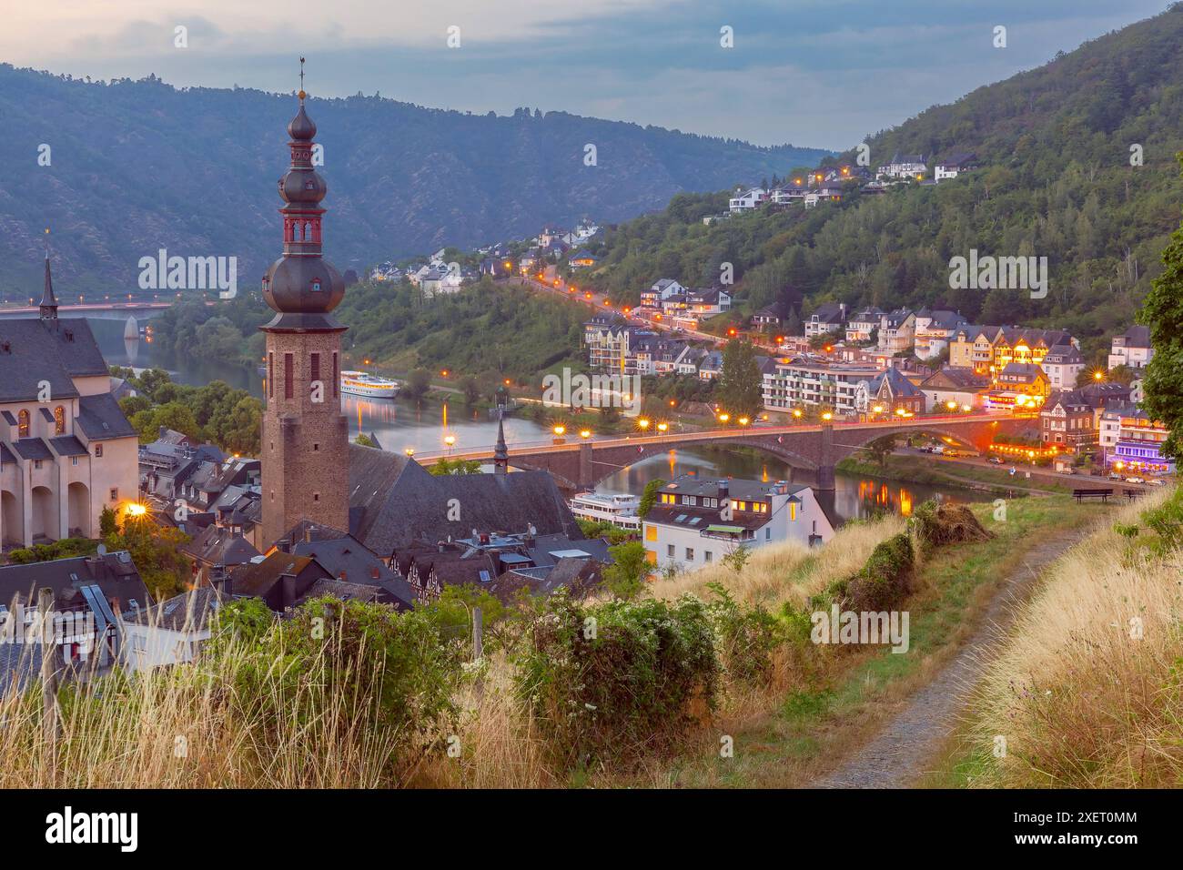 Vista al tramonto della città di Cochem con la sua chiesa, il ponte e le luci che si riflettono sul fiume Mosella, Germania Foto Stock