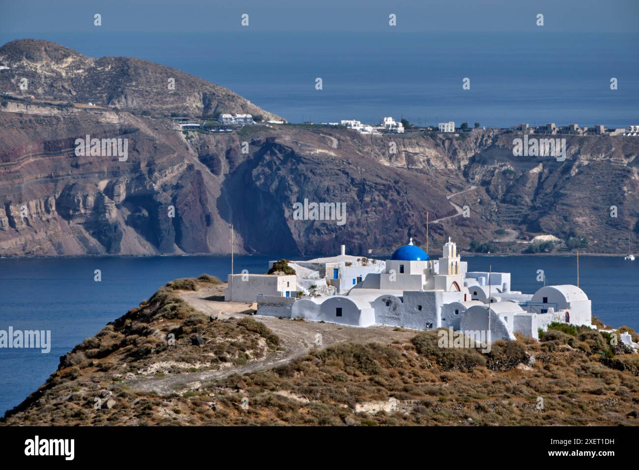 Il monastero di Moni Kimisi Theotokou sulla punta meridionale di Thirasia, con Santorini in lontananza. Isole Cicladi, Grecia. Foto Stock