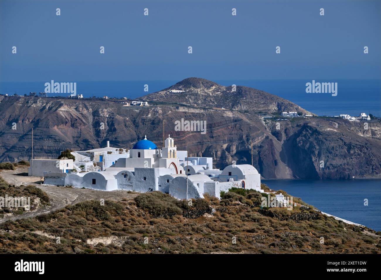 Il monastero di Moni Kimisi Theotokou sulla punta meridionale di Thirasia, con Santorini in lontananza. Isole Cicladi, Grecia. Foto Stock