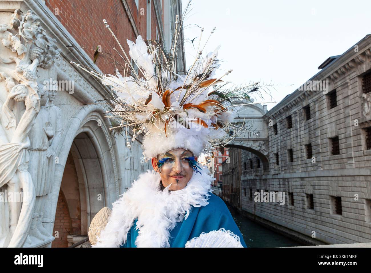 Carnevale di Venezia, uomo che indossa un copricapo elaborato con piume in posa al Ponte dei Sospiri, Venezia, Italia Foto Stock