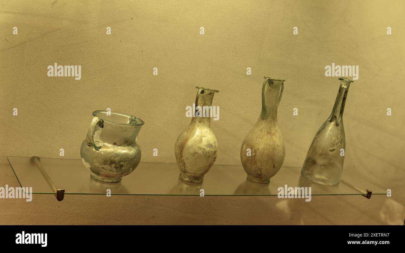 Un antico vaso di vetro verde romano dal design complesso. Presenta un corpo ampio, un collo stretto e manici decorativi che mostrano cra per la lavorazione del vetro romano Foto Stock