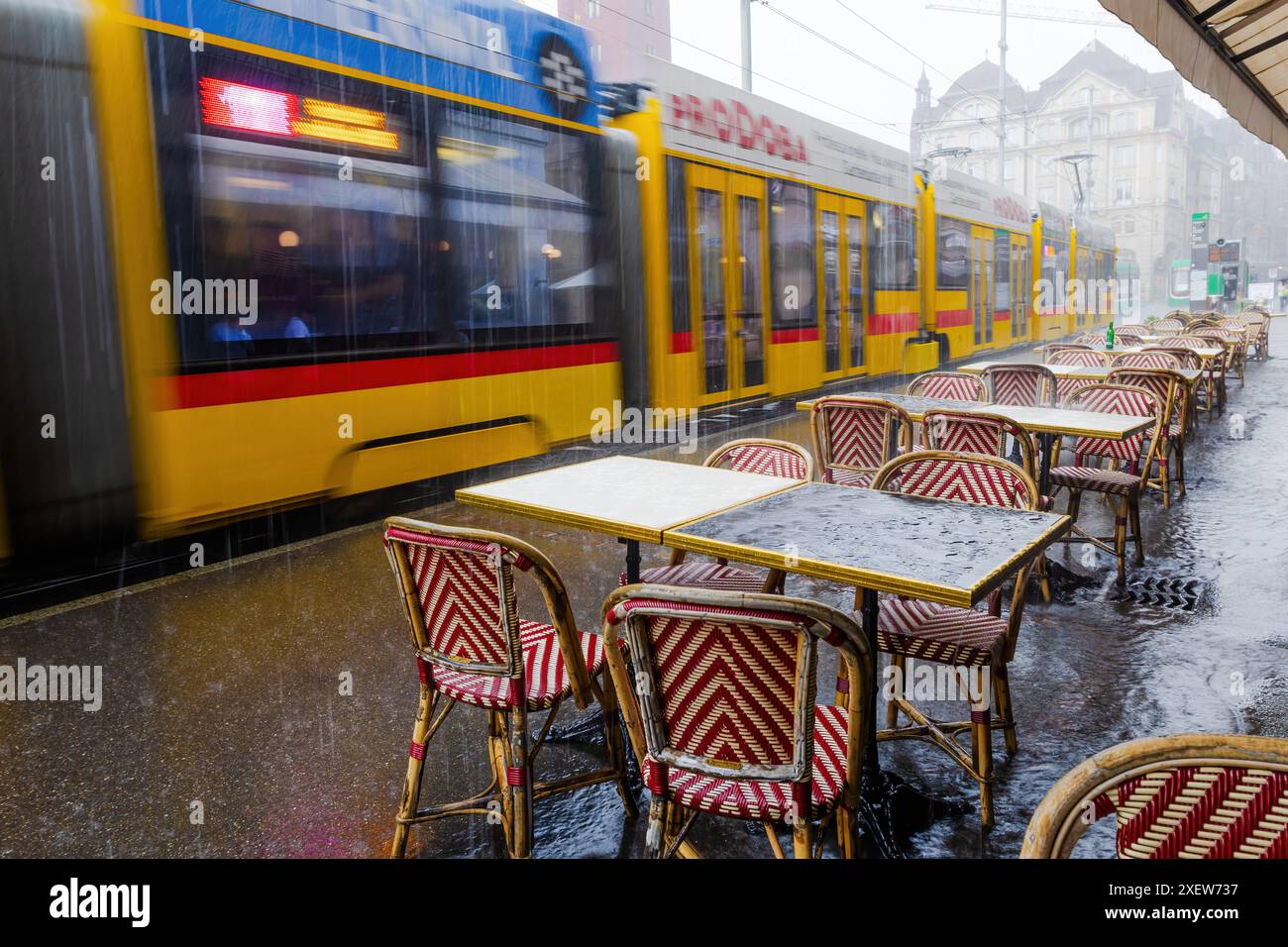 Un treno passa accanto a un ristorante con tavoli e sedie all'esterno. Le sedie sono rosse e gialle e i tavoli sono coperti da panni rossi e bianchi Foto Stock