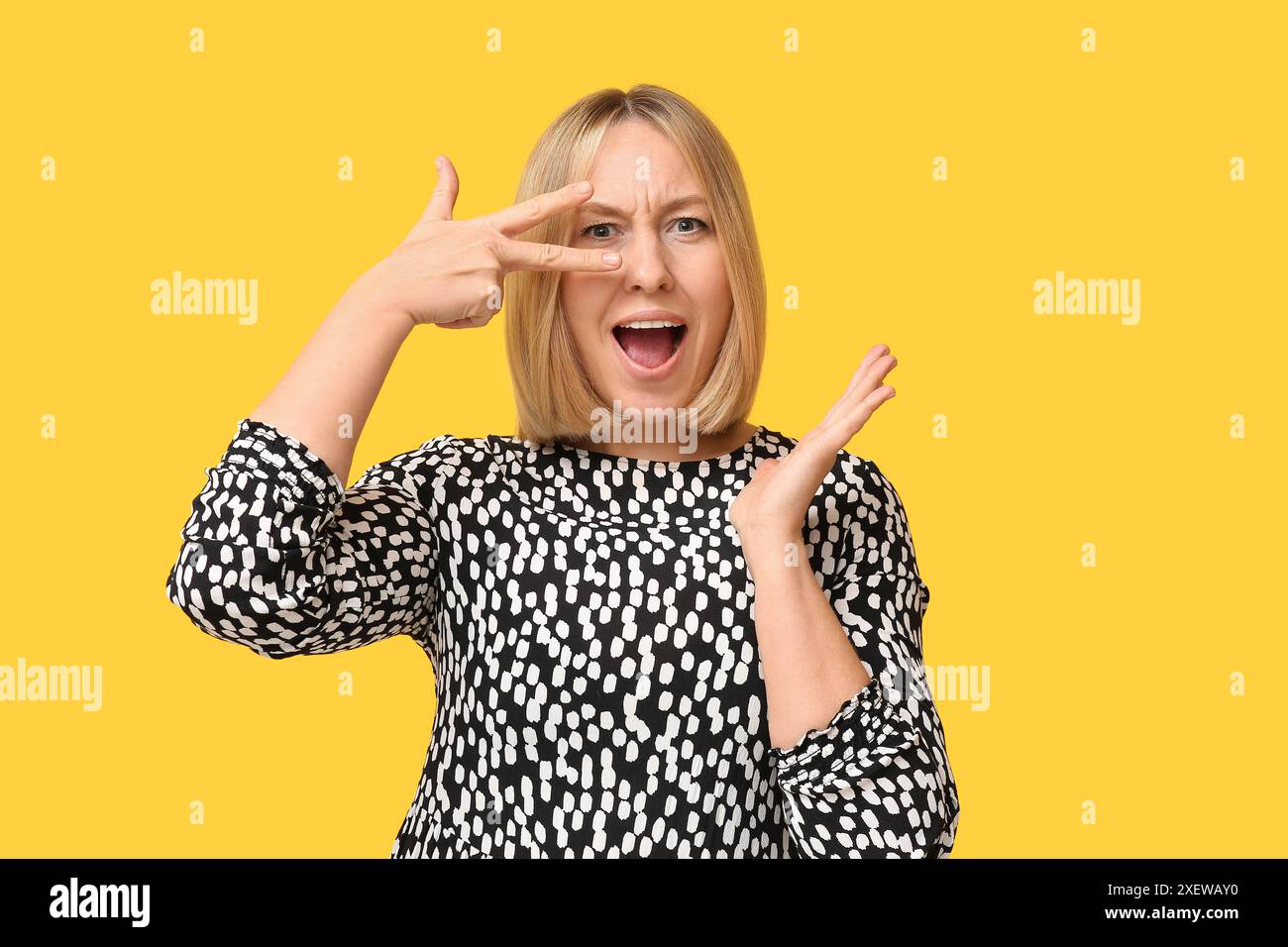 Bella giovane donna con acconciatura di Bob che mostra un gesto di vittoria su sfondo giallo Foto Stock