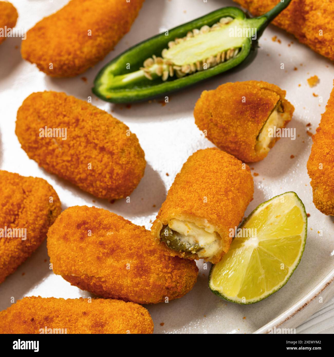 popper jalapeno ripieni di formaggio cremoso al forno con spicchi di lime e salsa al peperoncino dolce sul piatto, primo piano Foto Stock