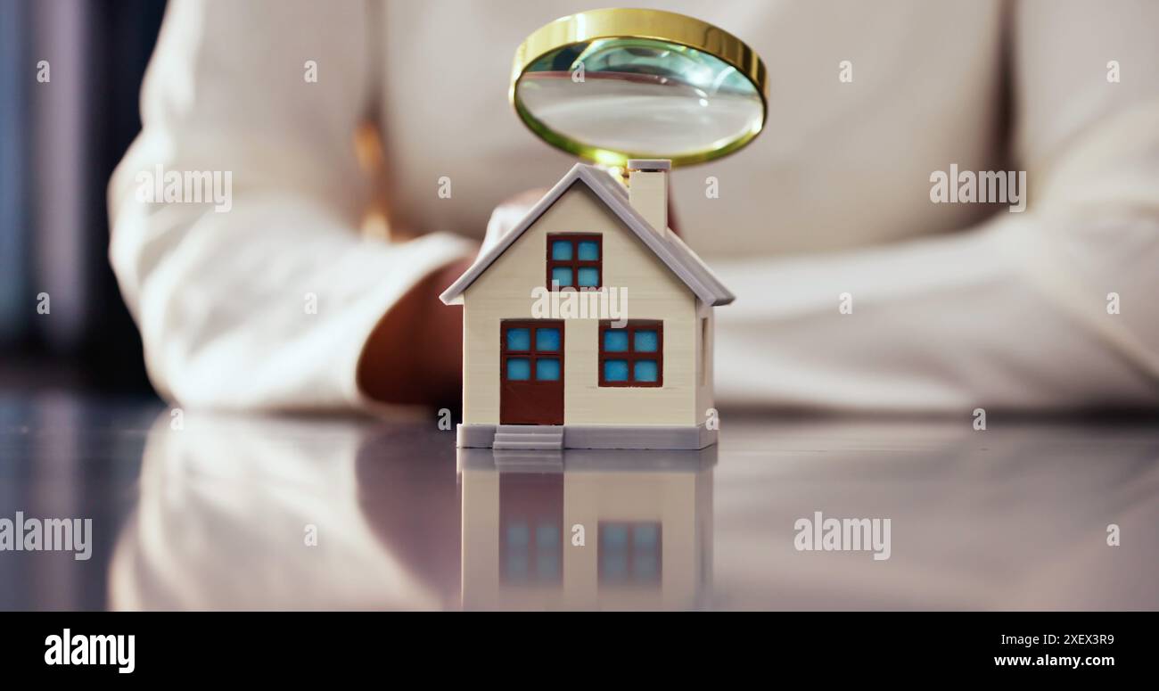 Donna afroamericana che ispeziona la casa con lente d'ingrandimento per la valutazione immobiliare e la valutazione delle tasse su laptop Foto Stock