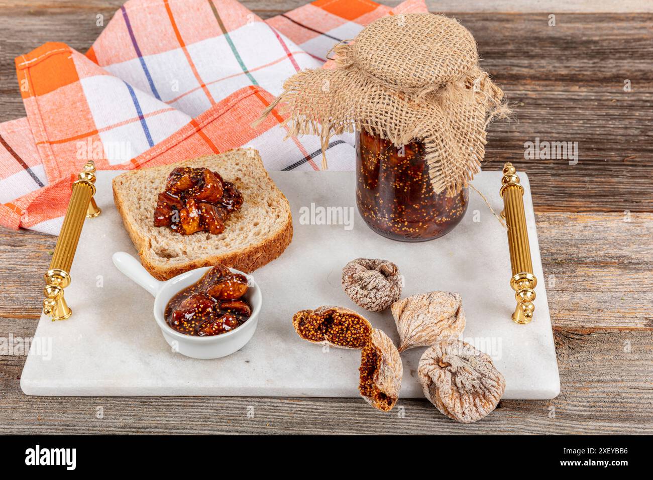 Composizione piatta con deliziosa marmellata di fichi su un tavolo di legno. Deliziosa marmellata di fichi in un vaso di vetro su un vassoio di marmo e confettura di fichi spalmata sul pane, distesa. Foto Stock