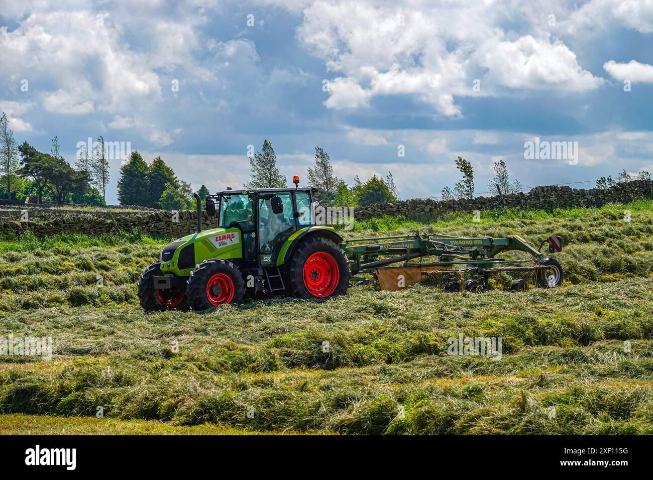 Trattore verde con ruote rosse che producono fieno in un campo alla periferia di Sheffield, South Yorkshire Foto Stock