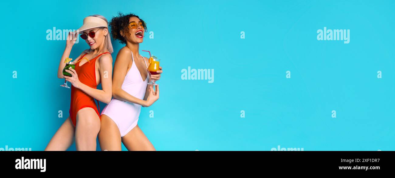 Due donne in costume da bagno bevono cocktail su sfondo blu Foto Stock