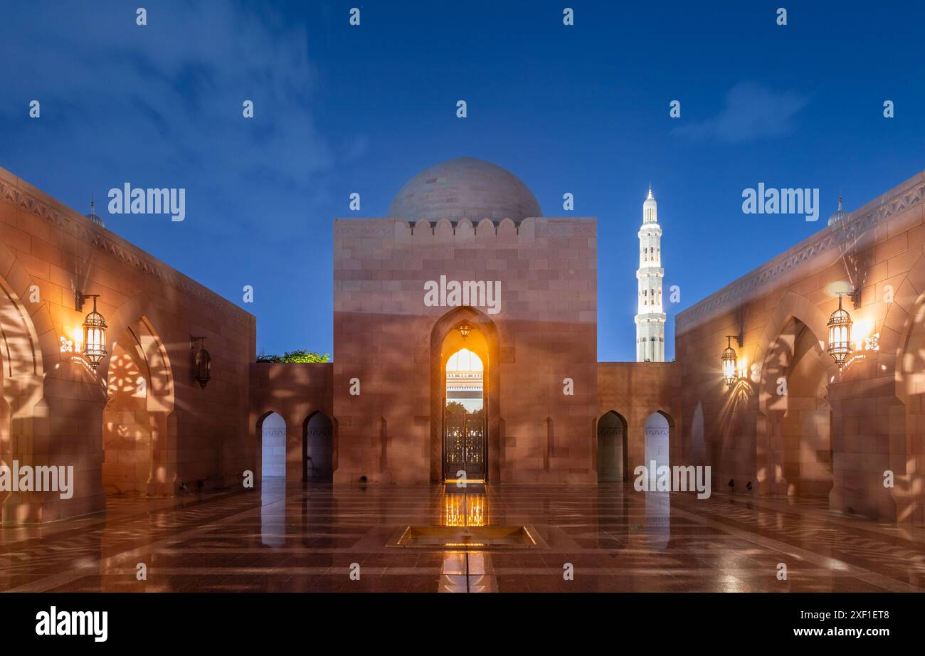 Cortile interno della grande Moschea del Sultano Qaboos, pareti decorate e minareto luccicante di notte, Mascate. Oman Foto Stock