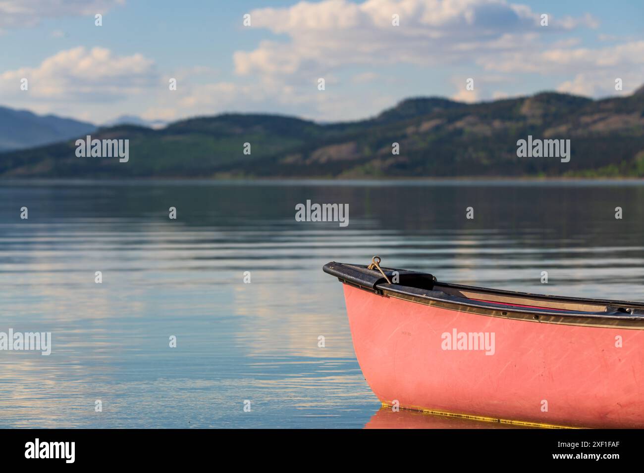 Vista estiva nel nord del Canada con vista sul lago e sulle montagne. Canoa rossa in vista a fuoco. Foto Stock