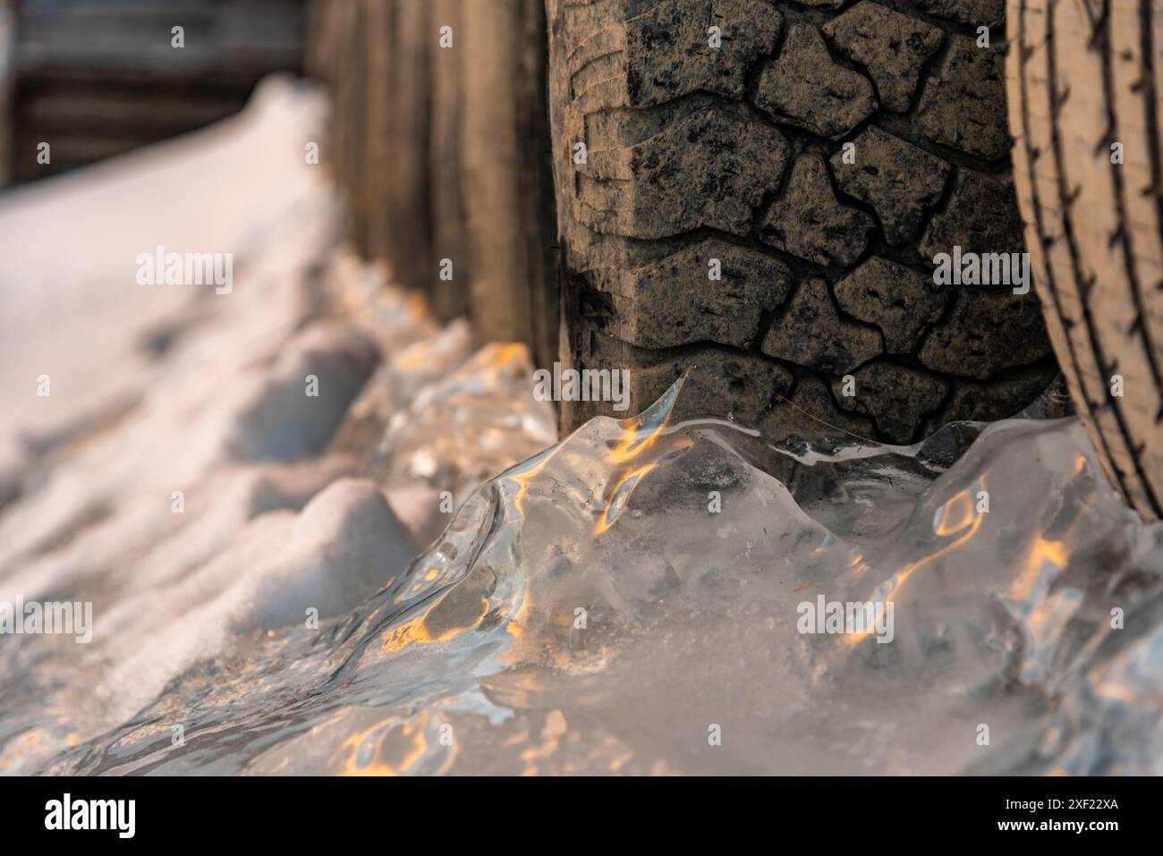 Grandi blocchi di ghiaccio ghiacciati su un porticciolo con pneumatici per auto in inverno. Il tramonto dorato si illumina sul lato di un lago gelido in inverno con il tramonto sullo sfondo. Foto Stock