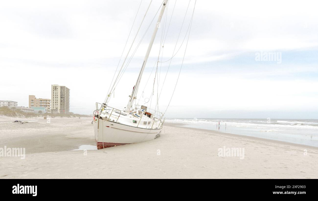 Scena drammatica di uno yacht arenato su una spiaggia sabbiosa dopo una distruttiva tempesta di uragano - Jacksonville, Florida USA 03.15.2024 Foto Stock