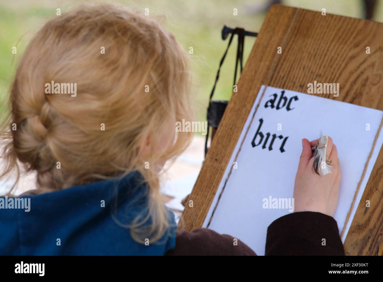 Una persona con capelli biondi sta praticando calligrafia, scrivendo l'alfabeto e la parola "uccello" in inchiostro nero su carta bianca. Stanno usando un calligrafo Foto Stock