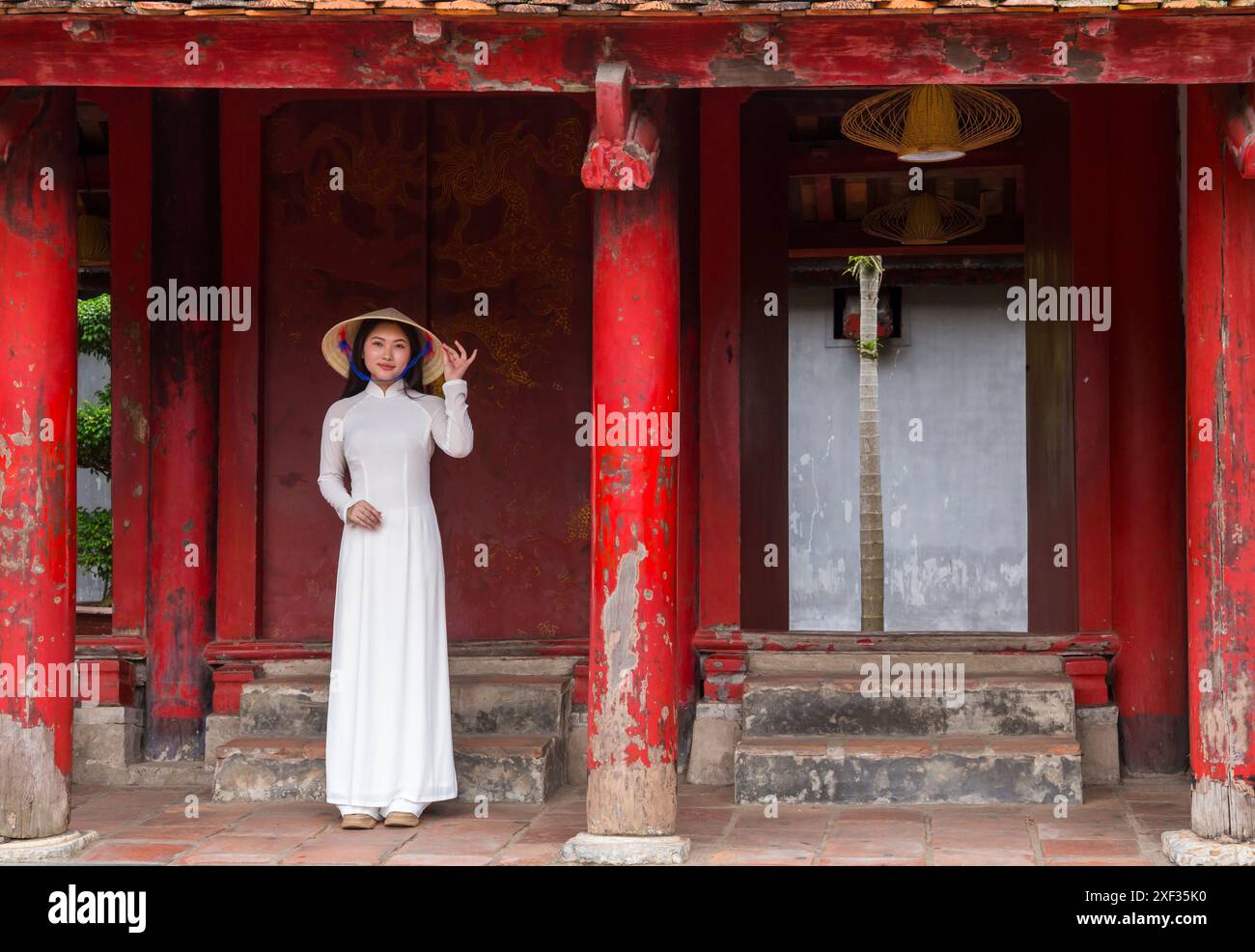 Graziosa giovane donna vietnamita che indossa la tradizionale tunica Ao dai e il cappello conico al Tempio della Letteratura di Hanoi, ha noi, Vietnam del Nord, Asia a giugno Foto Stock
