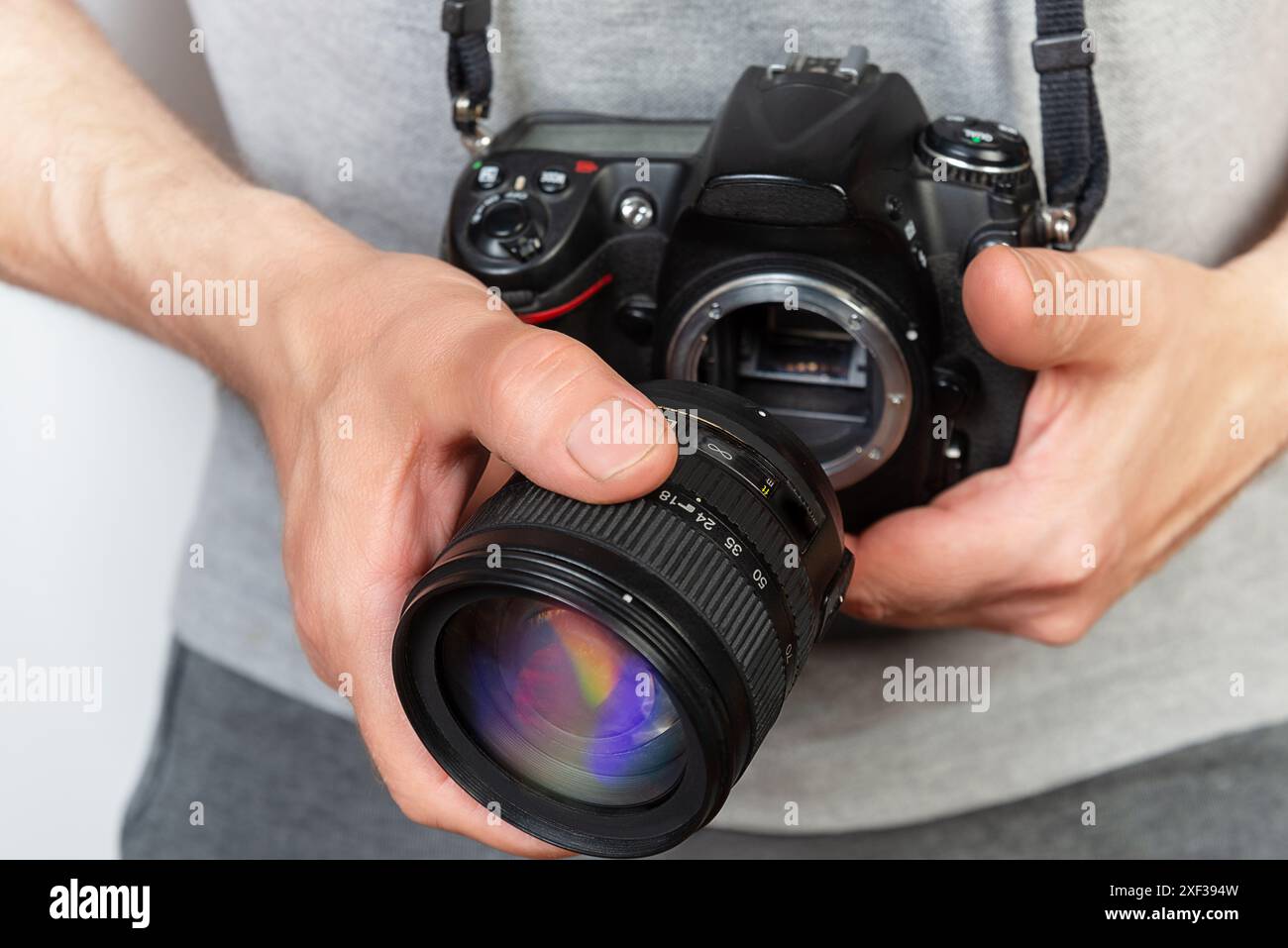 Primo piano di un fotografo che tiene in mano una fotocamera reflex digitale a obiettivo singolo (DSLR) e fissa l'obiettivo della fotocamera Foto Stock