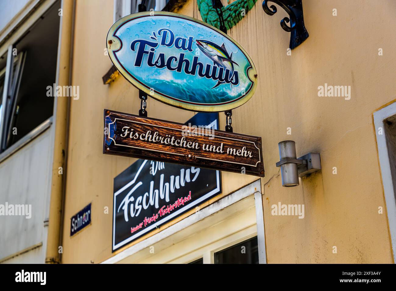 Un'insegna con la scritta "Dat Fischhuus – Fischbrötchen und mehr" (panini di pesce e altro) pende sopra l'ingresso di un negozio nel quartiere Schnoor di Brema, l'ex quartiere degli artigiani e degli operai della città. L'illustrazione mostra un pesce che salta sopra onde schiumose. Il negozio vende panini di pesce e altri piatti di frutti di mare da asporto. Wüstestätte, Brema, Germania. Foto Stock