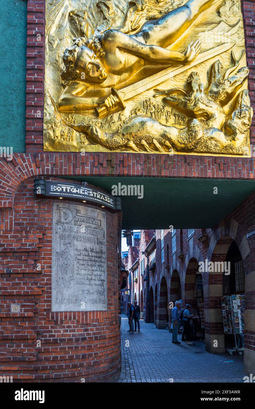 Il rilievo dorato "Der Lichtbringer" (“Il Portatore di Luce”) di Bernhard Hoetger corona l’ingresso di Böttcherstraße a Brema. Rappresenta un giovane armato di spada che si abbatte su una creatura simile a un drago a tre teste, circondato da una folla agitata e raggi di sole. Creato nel 1936, il rilievo era inteso come un omaggio a Hitler e rimane un monumento controverso dell’era nazista. Dopo il 1945, la figura è stata per lo più reinterpretata come l’arcangelo Michele. Sotto, una targa commemora la Casa Paula Becker-Modersohn. Böttcherstraße, Brema, Germania. Foto Stock