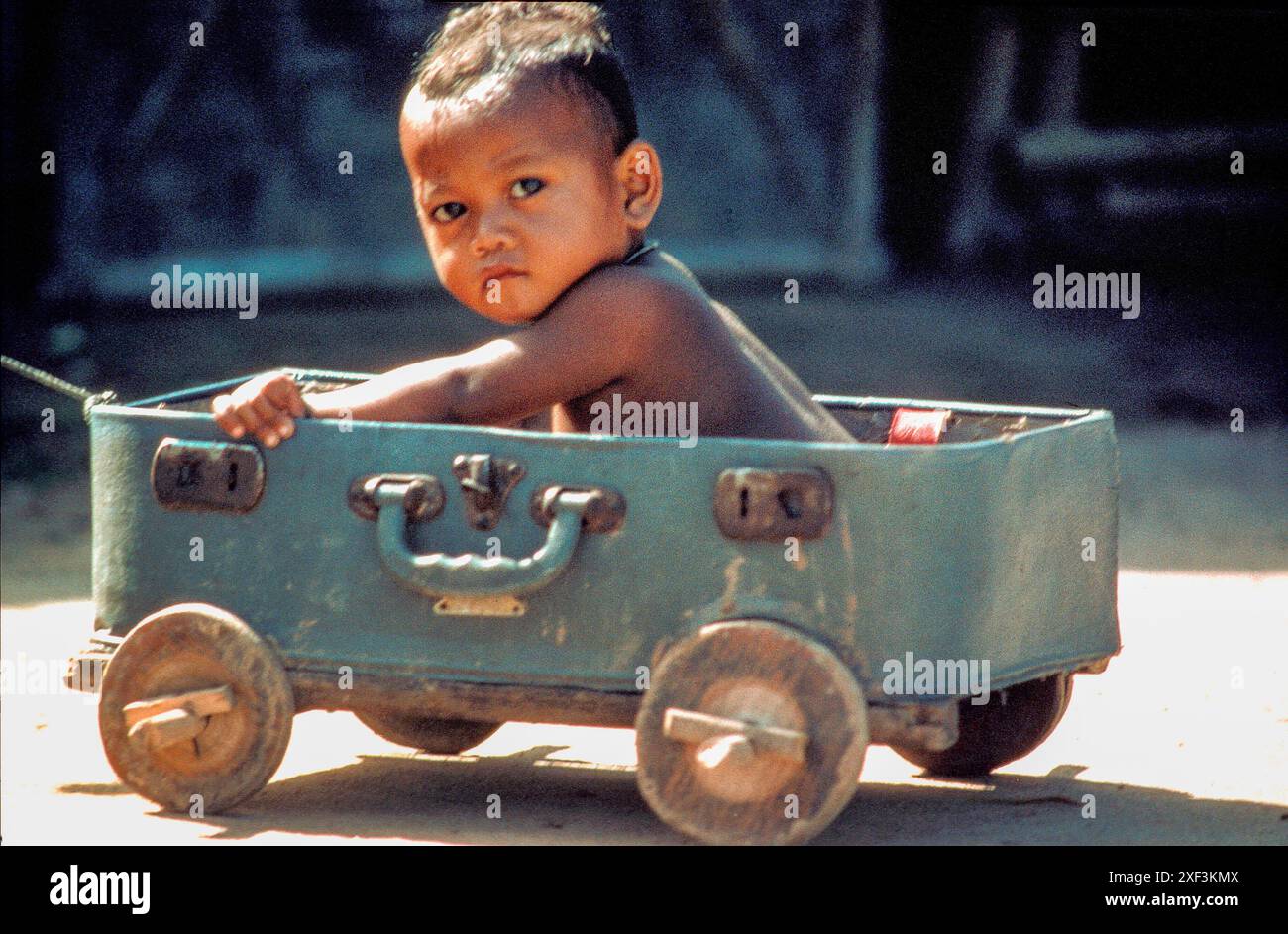 Thailandia. Il bambino gioca con un carrello fatto di valigia in un'area profughi nel nord-est. Foto Stock