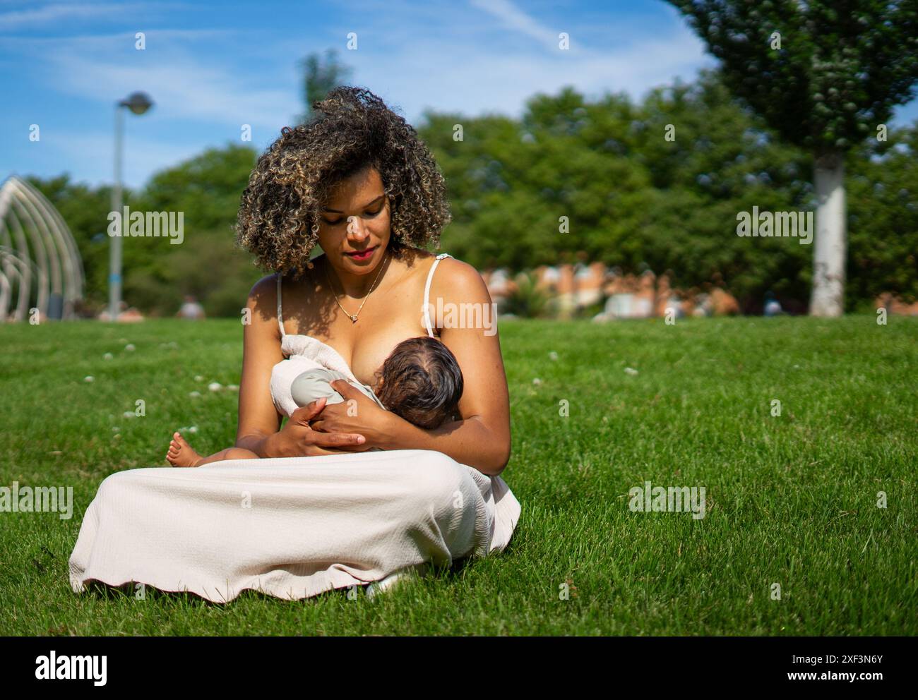 Madre latina con i capelli afro allattando il suo bambino in un parco Foto Stock