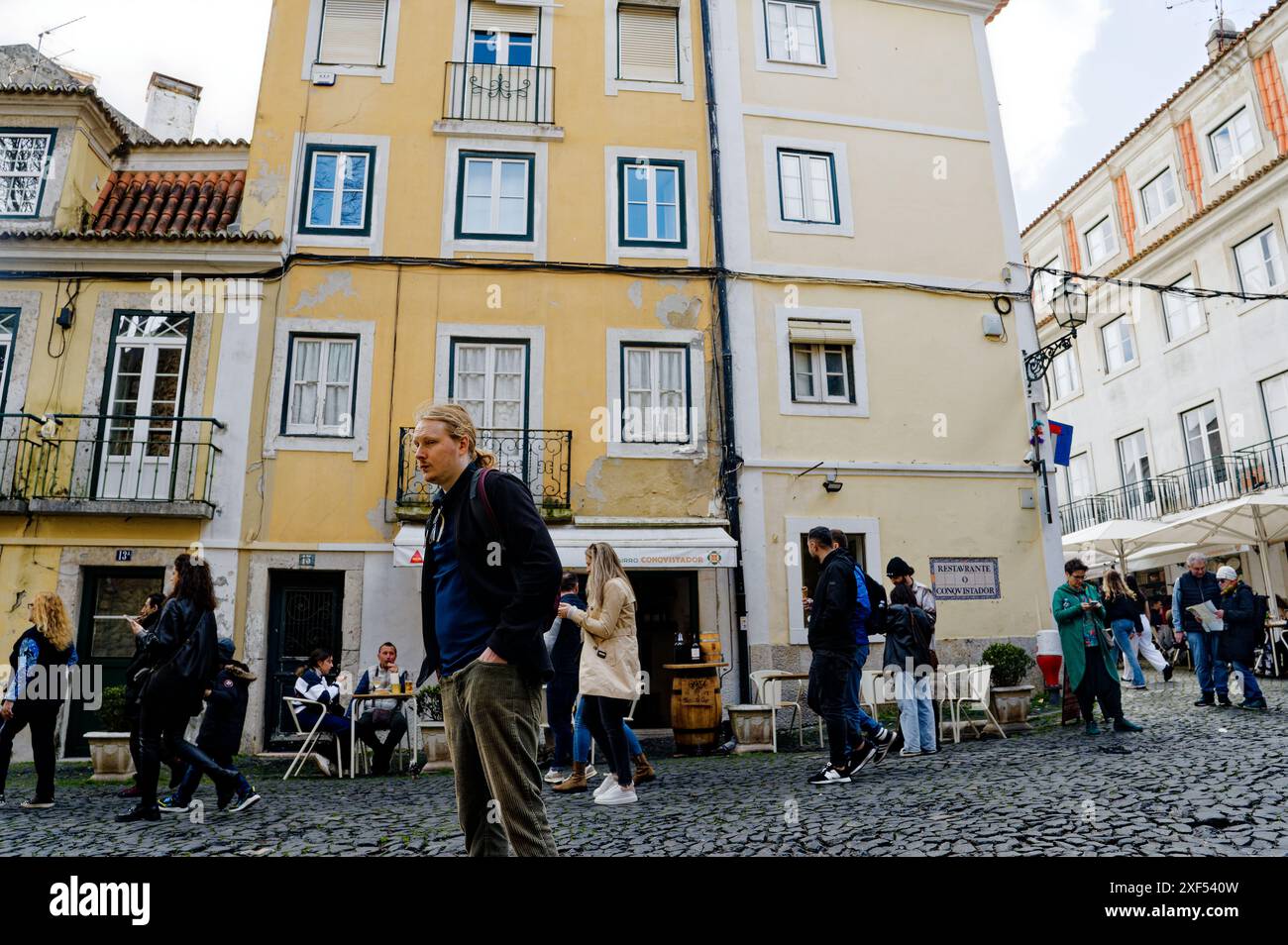 La gente si riunisce e cammina di fronte a un affascinante edificio giallo ad Alfama Foto Stock