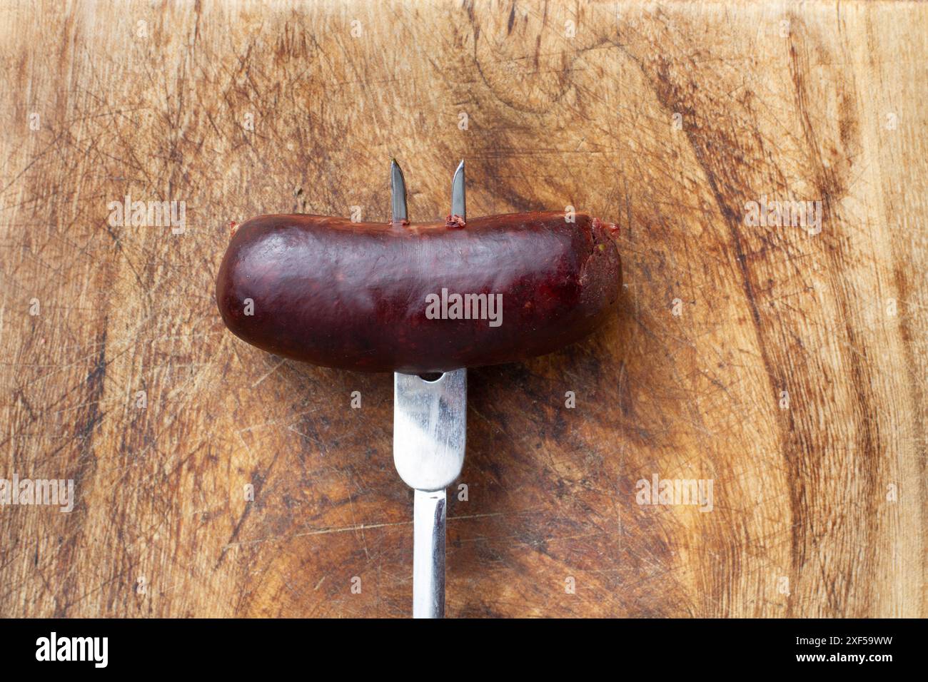 Una salsiccia di sangue spiedata su una forchetta su una tavola da cucina in legno con spazio per copiare Foto Stock